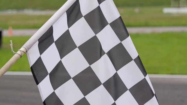 Checkered finish flag waving at racing track. Motorsport competition concept with finish line signal, speed, victory and race event outdoors.