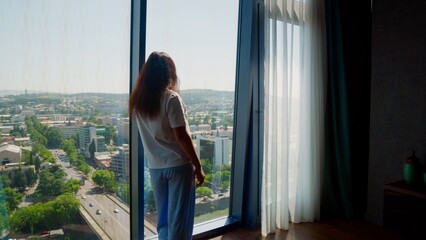 Woman gazing at city skyline from high rise apartment window © Andrei Burakov