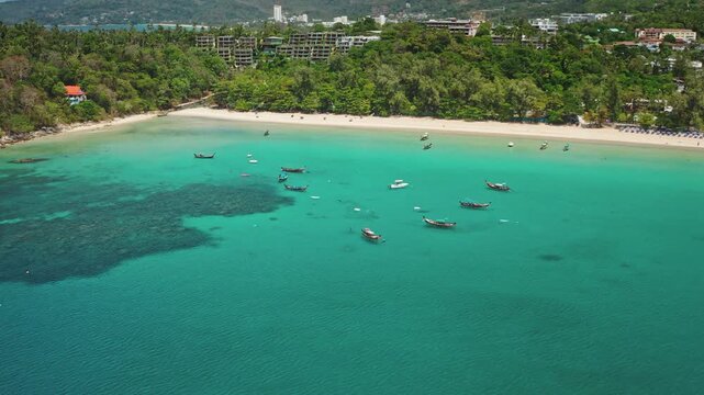 Stunning coastline of Phuket, Thailand, traditional longtail boats floating on the clear turquoise water near a sandy beach with lush green trees. Tropical vacation paradise. Aerial drone panorama