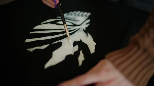 Close up of an artist adding finishing details to a white painted design on black fabric