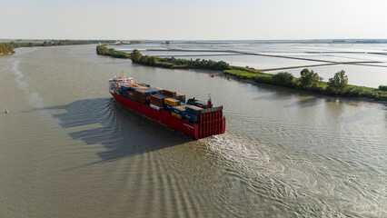 Obraz premium Container ship navigating Guadalquivir river past rice paddies
