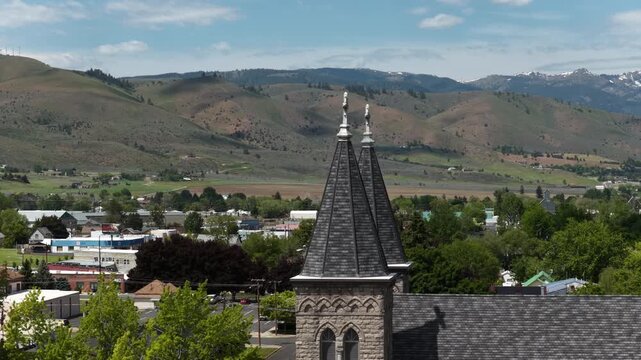 Aerial zoom shot of church steeple in Baker City Oregon in spring with Wallowa Mountains