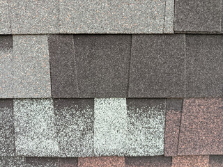 Fototapeta premium Detailed top-down view of overlapping asphalt roof shingles featuring a gritty, mineral-granule texture in various shades