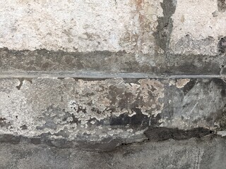 Fototapeta premium A close-up shot of a badly damaged concrete wall with a large hole, deep cracks, peeling plaster, and white liquid drip stains.