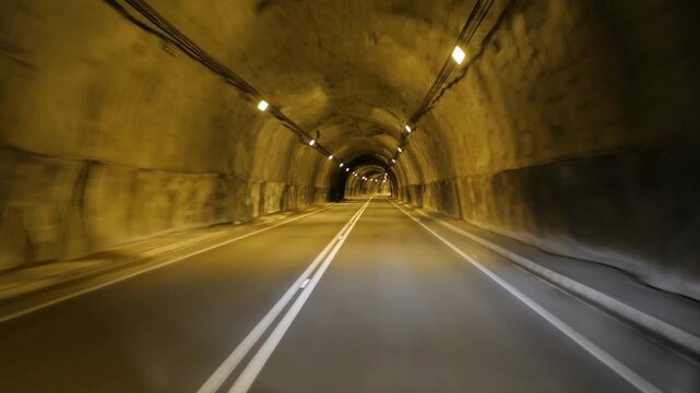 Underground stone tunnel with asphalt road, dark mountain cavern passage with warm lights, driving through a rocky subterranean highway