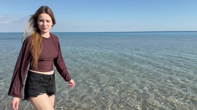 Young woman throwing stone skimming on sea water surface, back view of a girl playing and skipping stones on calm transparent ocean water on a sunny beach beach day