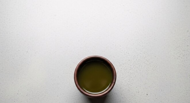 A small ceramic cup containing green tea leaves on a plain surface