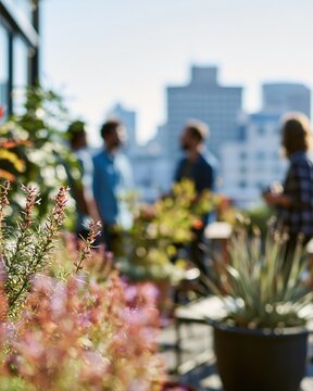 A focused medium shot of coworkers chatting on an office terrace blurred cityscape backdrop and vibrant plants highlighting a fresh and energetic work atmosphere.