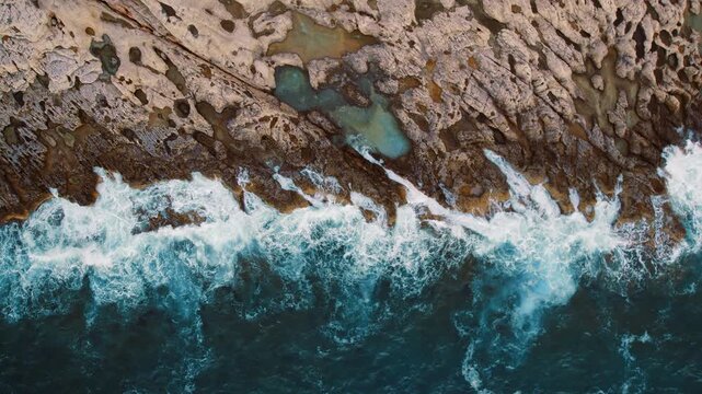 Tidal movement of sea waves fractures across a textured rocky coastline like white veins