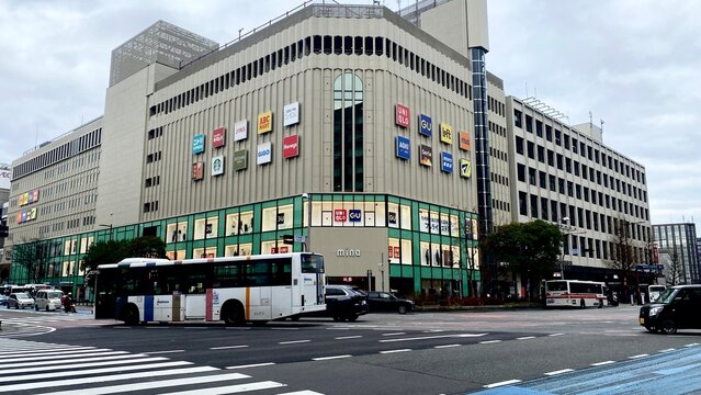 Modern commercial building with bus traffic and retail branding in a Japanese city