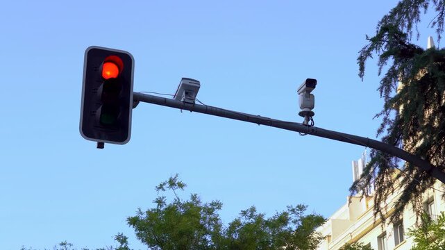 Detalle de un sem&aacute;foro cambiando de color junto a varias c&aacute;maras de vigilancia y control del tr&aacute;fico, con un cielo azul despejado de fondo.