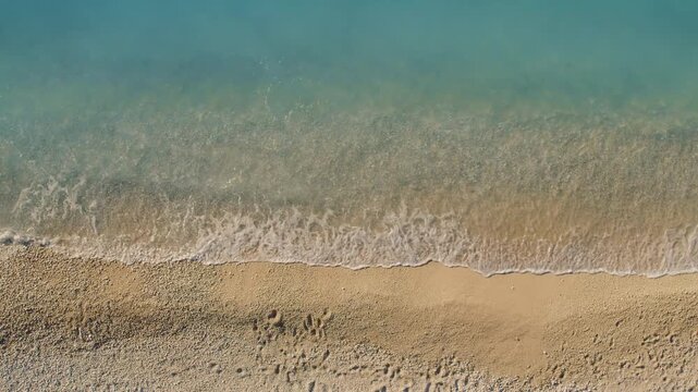 Gentle wave lapping onto golden beach on a calm sunny summer day in Greece