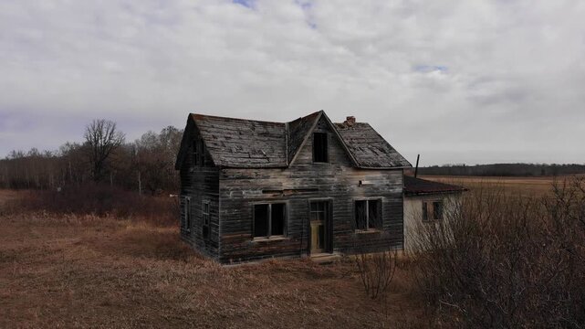 Drone moving towards ans then over abandoned old wooden farmhouse on a cloudy day
