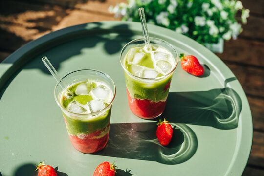 Refreshing strawberry matcha lattes served outdoors in natural sunlight. Modern healthy drink and summer refreshment concept