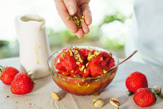 Sprinkling chopped pistachios over homemade strawberry sorbet. Preparing refreshing summer dessert with fresh ingredients