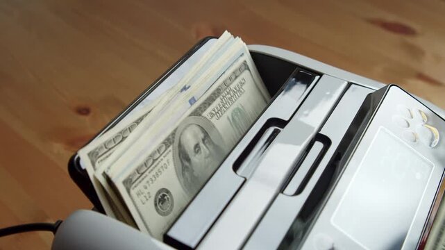A person feeds a stack of dollars into a modern counting machine. The machine swiftly organizes the cash, displaying a seamless counting process in a warm office atmosphere