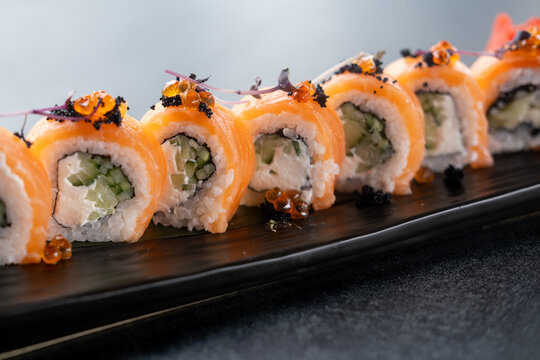 Salmon roll. Seafood dish. Row sushi rice with nori cream cheese cucumber masago roe on black platter. Oriental menu meal with herb sprouts.