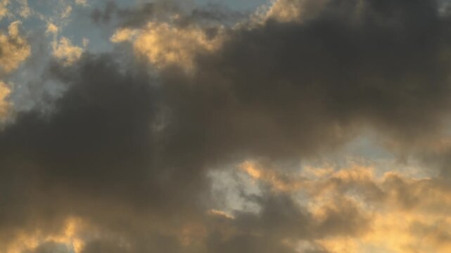 Timelapse of golden evening clouds drifting across a blue sky

