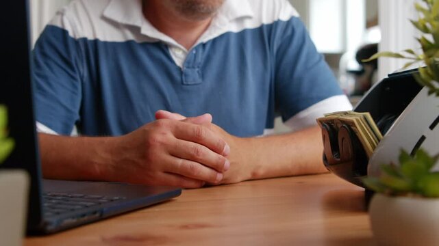 A person carefully counts crisp bills on a wooden desk surrounded by plants, basking in soft sunlight that fills the cozy workspace with warmth