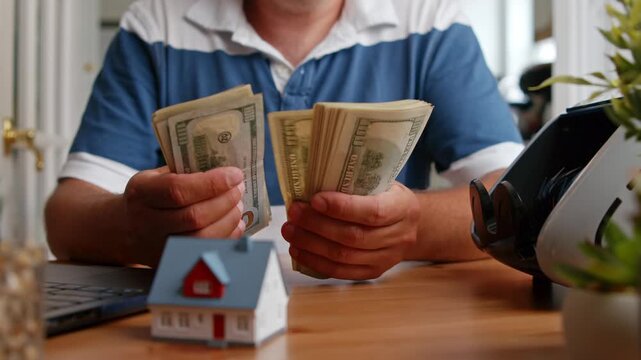 Hands carefully sort through stacks of cash while a small house model sits nearby, symbolizing future investments and dreams during a quiet afternoon