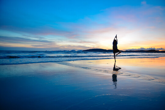 Single Asian girl doing yoga with background of dramatic evening glow during sunset, photo taken on Ao Nang beach, Krabi, Thailand.