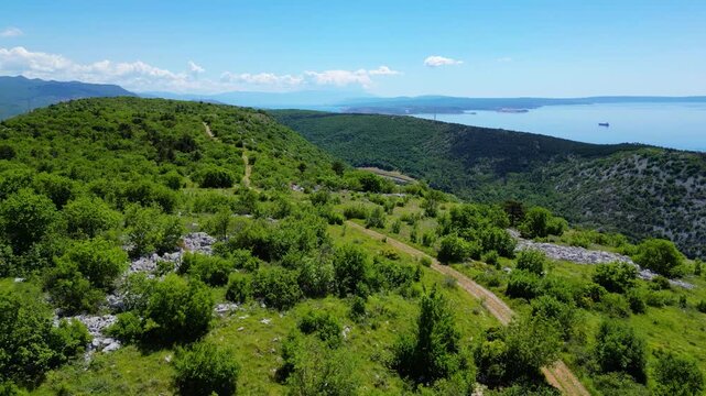 Expansive aerial view of Rijeka, Croatia, showcasing the vibrant port city, Adriatic Sea, and lush coastal hills under a bright, partly cloudy sky.
