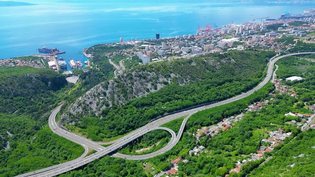 Aerial view of Rijeka, Croatia, showcasing its vibrant port, sprawling city, and intricate highway nestled between lush hills and the sparkling Adriatic Sea.