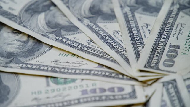 Richly designed hundred dollar bills are beautifully spread across a textured surface, shimmering under warm light, creating an atmosphere of prosperity and success