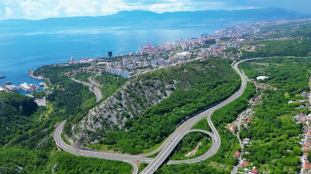 Drone shot of a major highway intersection cutting through verdant Croatian landscape, with a charming village nestled in the hills. A blend of progress and nature.