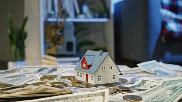 Small houses rest on a bed of cash, hinting at dreams of ownership and investment. Bright light illuminates the scene, reflecting hopes in a bustling real estate market