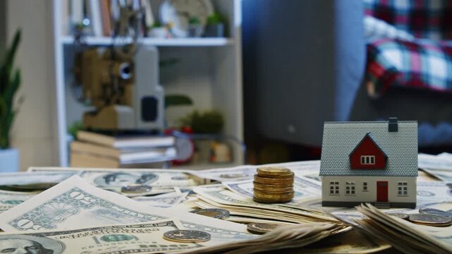 Discover the intricate relationship between real estate and finance as miniature houses rest atop stacks of dollar bills, bringing dreams of homeownership to life