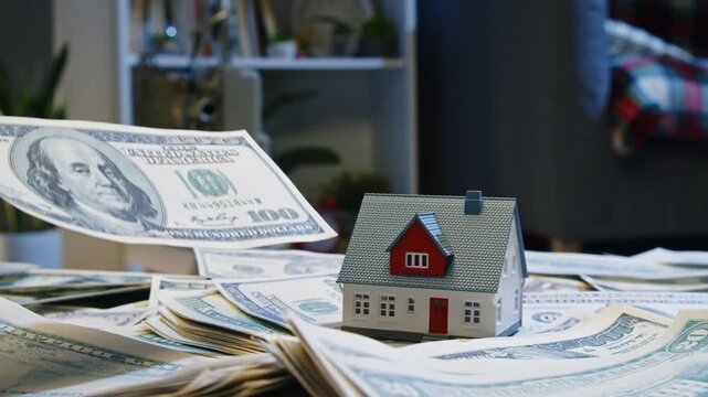 Miniature house sits atop a pile of money, symbolizing the bond between property investment and financial growth in a comfortable indoor space