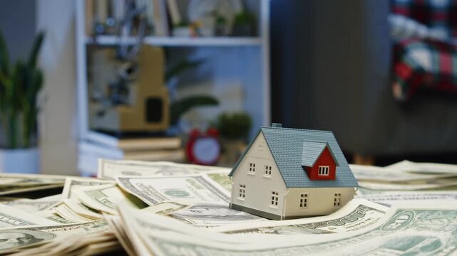Discover the dynamic interplay of money and real estate as a small house model rests on a bed of cash in a warm and inviting space
