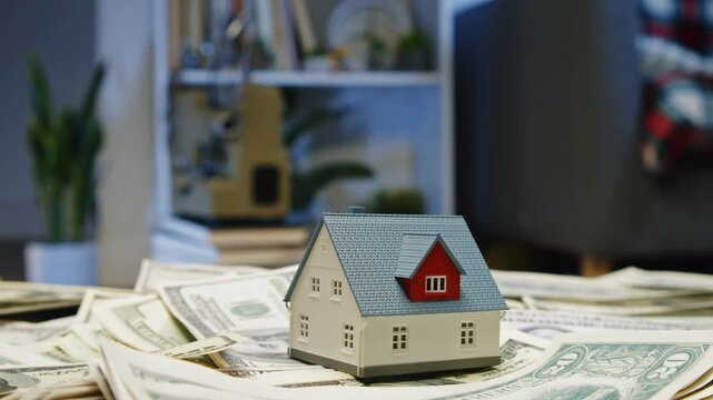 Miniature houses rest on a mountain of cash, symbolizing dreams of homeownership and investment opportunities. A cozy, modern setting enhances this financial vision