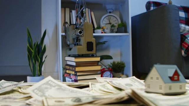 In a stylish office filled with books and greenery, dollar bills create a soft bed for a tiny model house, evoking dreams of prosperity and comfort