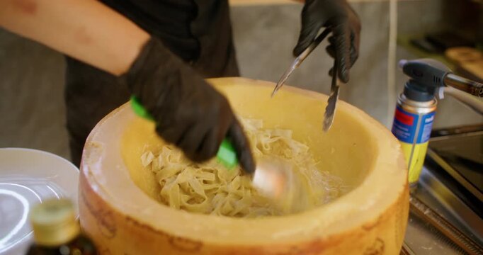 Pasta preparation. Italian cuisine. Chef mixing hot parmesan cheese wheel with melted creamy sauce making tasty gourmet dish.