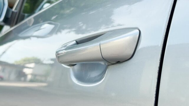 A hand opens a silver door on a modern car outside. The motion makes a sharp clicking and heavy slamming sound.