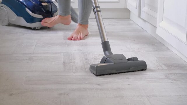 Barefoot woman cleaning kitchen floor with a modern vacuum cleaner