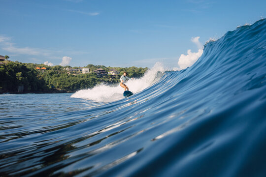 Surfer girl rides crashing ocean wave in sunny day in Bali