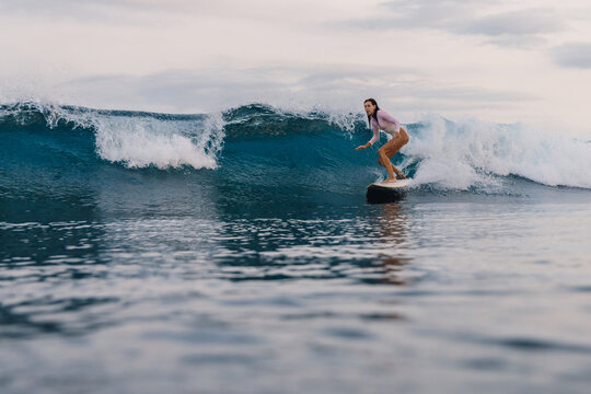 Surfer girl riding on blue wave on surfboard in ocean, aquatic sport