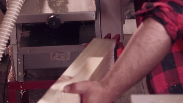 Carpenter occupation. lumber planer. Man in red plaid shirt smoothing wood with clamp on professional electric machine with sawdust.