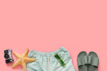 Naklejka premium Swimming trunks with beach accessories and photo camera on pink background