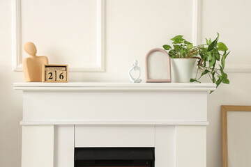 Obraz premium Blank frame with plant, statuettes and cube calendar on fireplace near light wall
