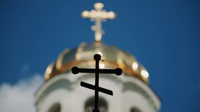 Foreground silhouette of a Christian cross with a softly blurred church dome and golden cross in the background