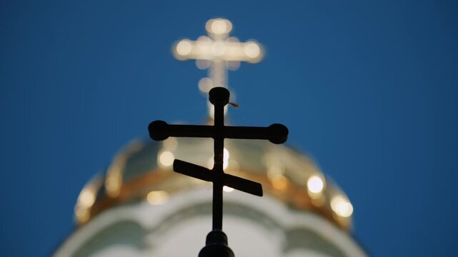 Foreground silhouette of a Christian cross with a softly blurred church dome and golden cross in the background