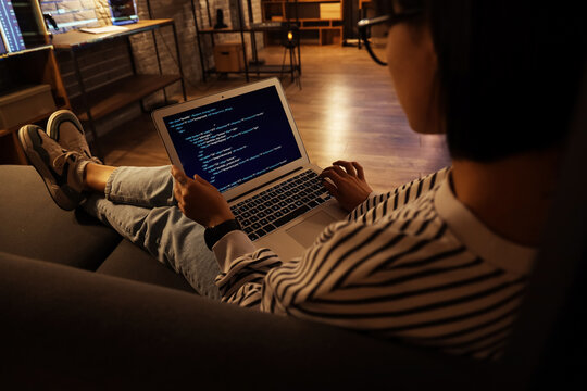 Female programmer working with laptop on couch in office at night, closeup