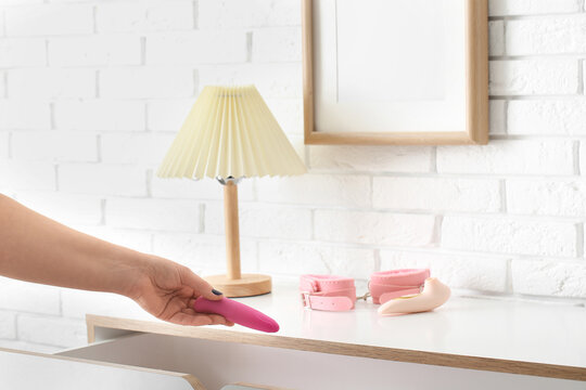 Woman taking vibrator from chest of drawers in room