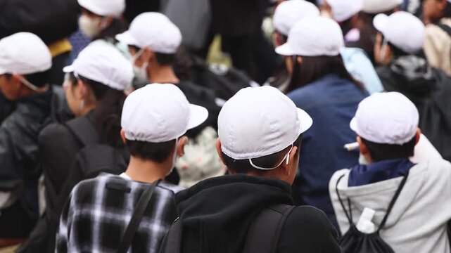 Group of school children students outdoor excursion, guided tour in the city with guide, docent with tourist pupils visitors, wear color caps hats, kids class field trip, urban sightseeing in Japan