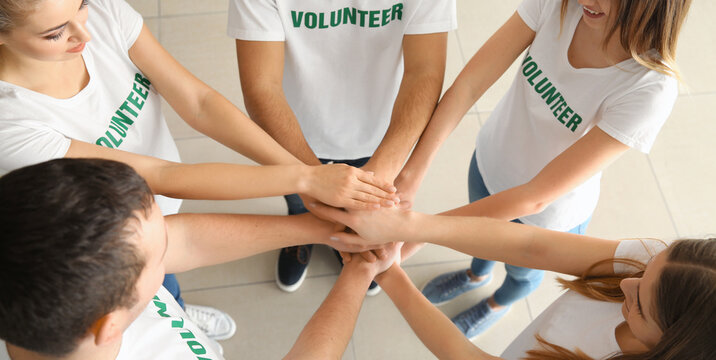Team of young volunteers putting hands together indoors
