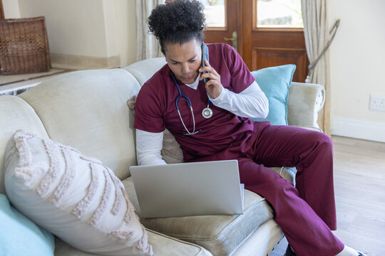 Silver laptop and smartphone are sitting on beige sofa near stethoscope and pillows